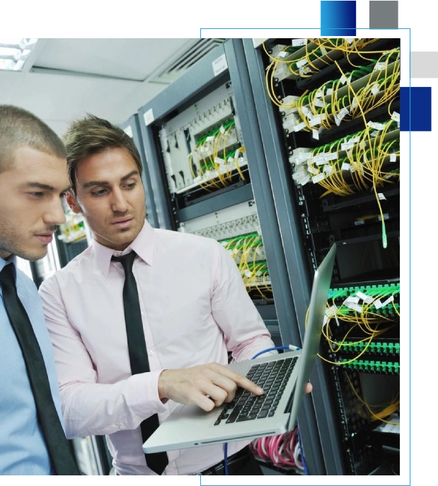 Two men looking at a laptop in front of server racks.